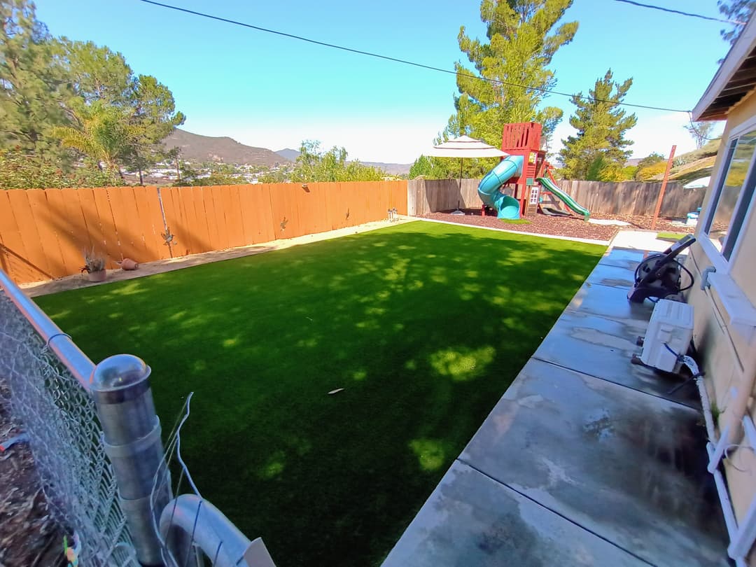 wide angle view of backyard with artificial turf and playground